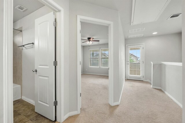 hall with visible vents, baseboards, attic access, and carpet flooring