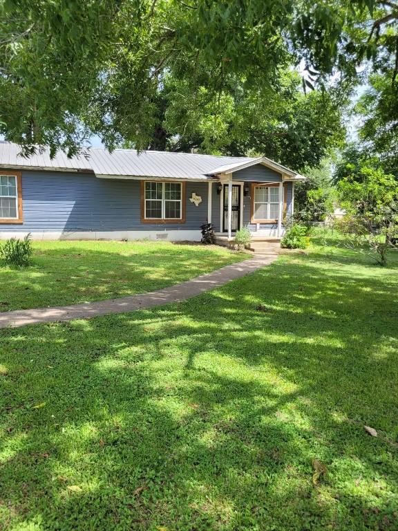 ranch-style house featuring covered porch, a front yard, and metal roof