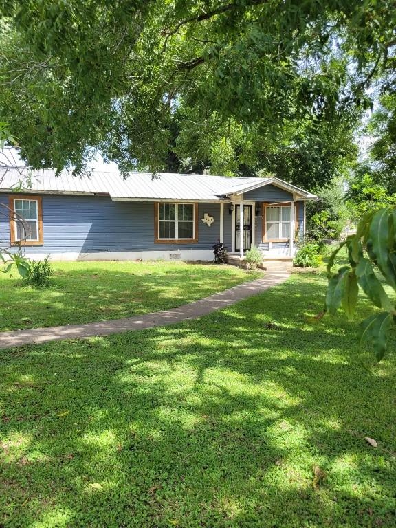 ranch-style home with metal roof, a front yard, and a porch