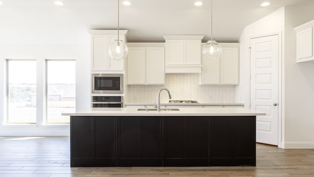 kitchen with oven, black microwave, a center island with sink, sink, and white cabinetry