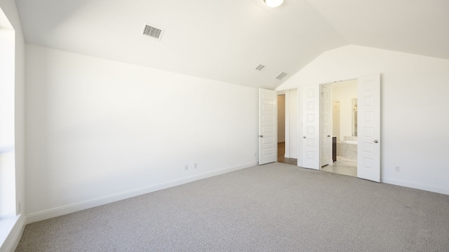 unfurnished bedroom with ensuite bathroom, lofted ceiling, and light colored carpet