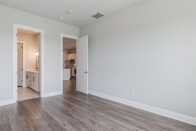 4507 E Martin Luther King Jr Blvd Unit 122, Austin, TX 78721 - unfurnished bedroom with stainless steel refrigerator with ice dispenser, wood finished floors, baseboards, and ensuite bath