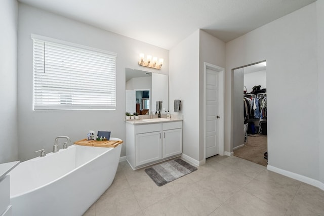 full bath featuring baseboards, a walk in closet, a freestanding bath, and vanity