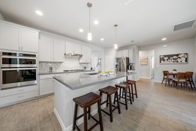 kitchen featuring hanging light fixtures, white cabinetry, a kitchen island with sink, and appliances with stainless steel finishes