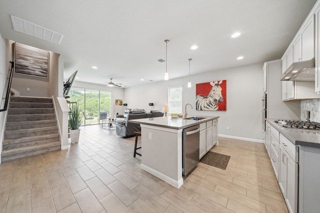 kitchen featuring a center island with sink, appliances with stainless steel finishes, open floor plan, white cabinetry, and under cabinet range hood