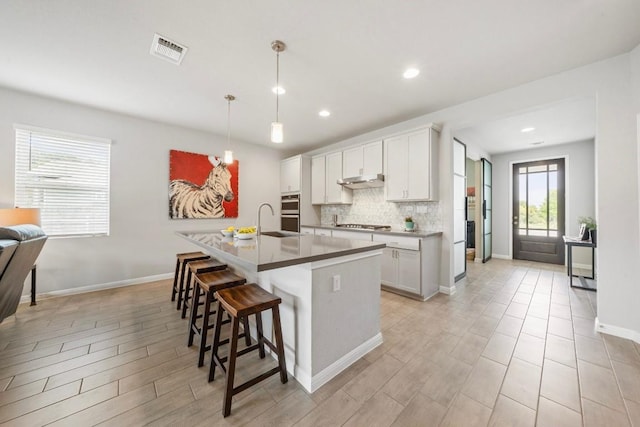 kitchen featuring decorative light fixtures, a breakfast bar area, decorative backsplash, white cabinets, and an island with sink