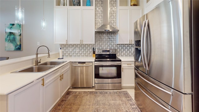 kitchen featuring wall chimney range hood, sink, appliances with stainless steel finishes, hanging light fixtures, and white cabinets