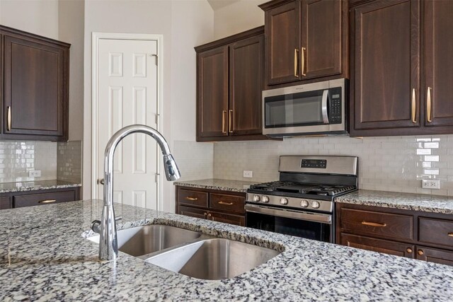 kitchen featuring stainless steel appliances, light stone countertops, sink, decorative backsplash, and dark brown cabinetry