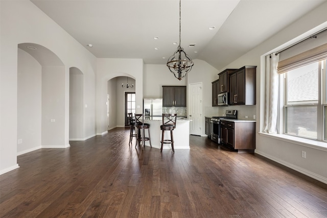 kitchen with a kitchen breakfast bar, appliances with stainless steel finishes, a kitchen island with sink, dark wood-type flooring, and dark brown cabinetry