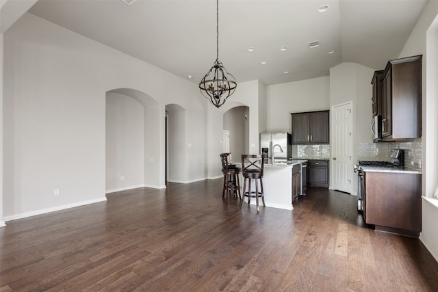 kitchen with appliances with stainless steel finishes, dark wood-type flooring, an island with sink, and a kitchen breakfast bar