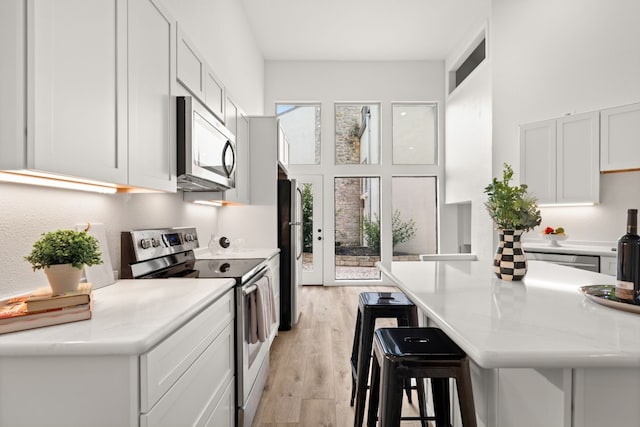 1 Crystal Springs Ct Unit G, The Hills, TX 78738 - kitchen with stainless steel appliances, light countertops, a breakfast bar area, light wood finished floors, and a towering ceiling