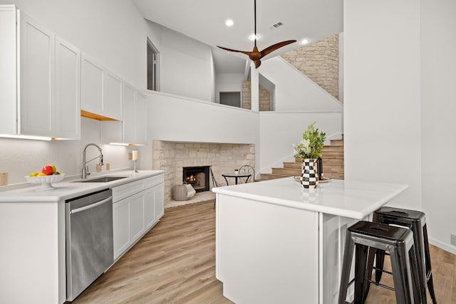 1 Crystal Springs Ct Unit G, The Hills, TX 78738 - kitchen featuring stainless steel dishwasher, white cabinets, a breakfast bar, a stone fireplace, and light wood-type flooring