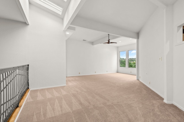 unfurnished living room featuring a ceiling fan, a skylight, beam ceiling, baseboards, and carpet