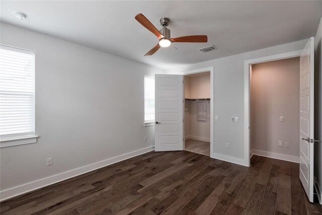 unfurnished bedroom featuring dark wood-type flooring, a spacious closet, a closet, and ceiling fan