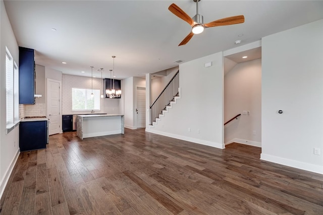 unfurnished living room with ceiling fan with notable chandelier and dark wood-type flooring