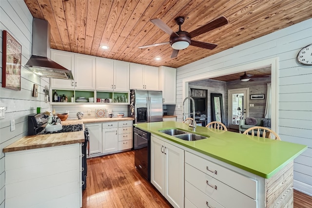 kitchen with stainless steel fridge, light hardwood / wood-style flooring, wall chimney exhaust hood, and a center island with sink