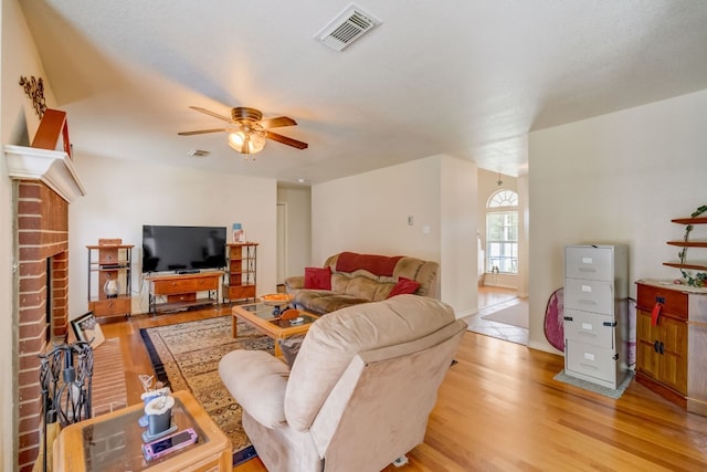 living room with ceiling fan, a fireplace, and light wood-type flooring