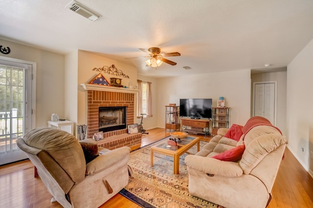 living room featuring ceiling fan, a fireplace, light hardwood / wood-style floors, and a healthy amount of sunlight