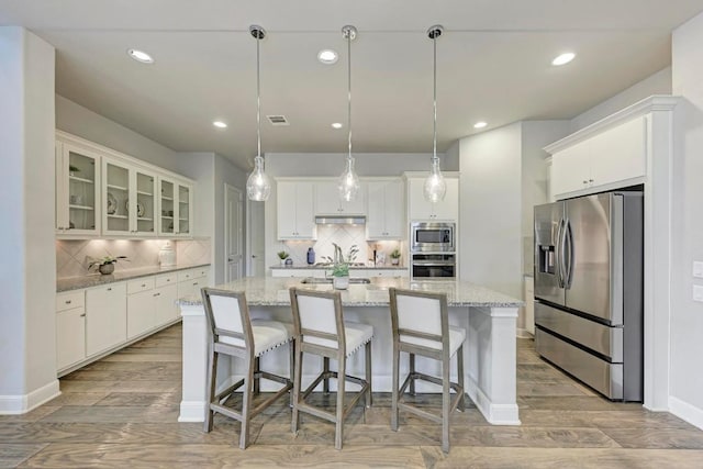 kitchen featuring decorative light fixtures, stainless steel appliances, decorative backsplash, a kitchen island, and light hardwood / wood-style flooring