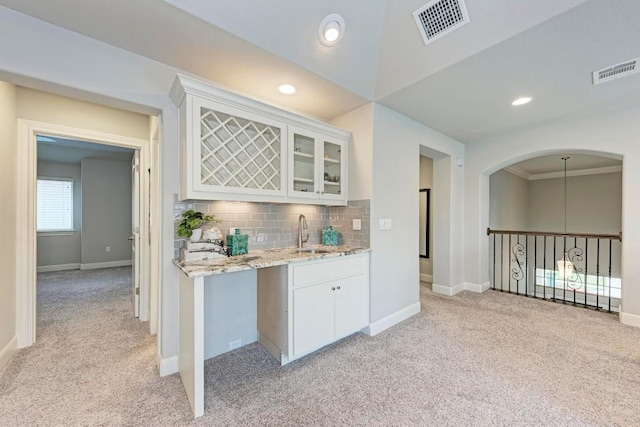 kitchen featuring tasteful backsplash, white cabinets, ornamental molding, sink, and light colored carpet