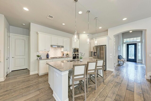 kitchen with tasteful backsplash, stainless steel appliances, a center island with sink, white cabinetry, and wood-type flooring