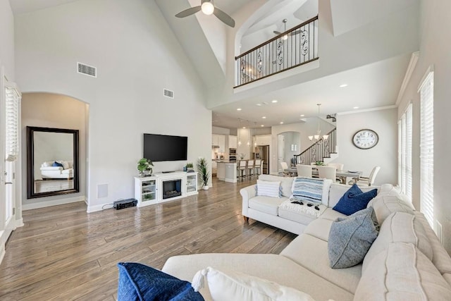 living room with a fireplace, a high ceiling, ceiling fan with notable chandelier, wood-type flooring, and ornamental molding