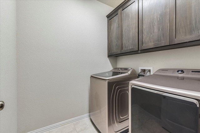 clothes washing area with cabinets, light tile patterned floors, and washer and clothes dryer