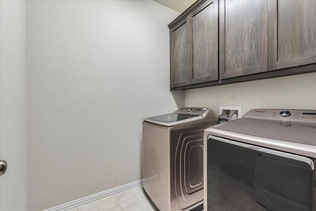 clothes washing area featuring washing machine and dryer, cabinet space, baseboards, and light tile patterned floors