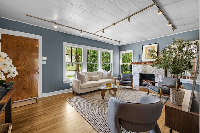 living room featuring rail lighting, wood finished floors, a baseboard radiator, and a lit fireplace