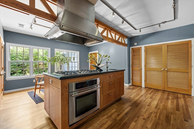 kitchen featuring dark countertops, visible vents, island range hood, appliances with stainless steel finishes, and wood finished floors