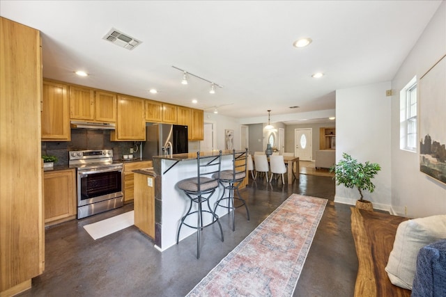 kitchen featuring rail lighting, an island with sink, stainless steel appliances, pendant lighting, and a kitchen bar