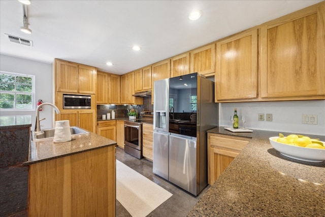 kitchen featuring stainless steel appliances, rail lighting, sink, dark stone countertops, and a kitchen island