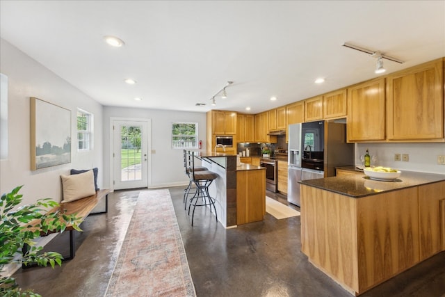 kitchen with appliances with stainless steel finishes, a breakfast bar area, dark stone counters, a kitchen island, and rail lighting