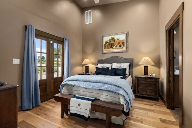 bedroom featuring light hardwood / wood-style flooring, french doors, and a towering ceiling