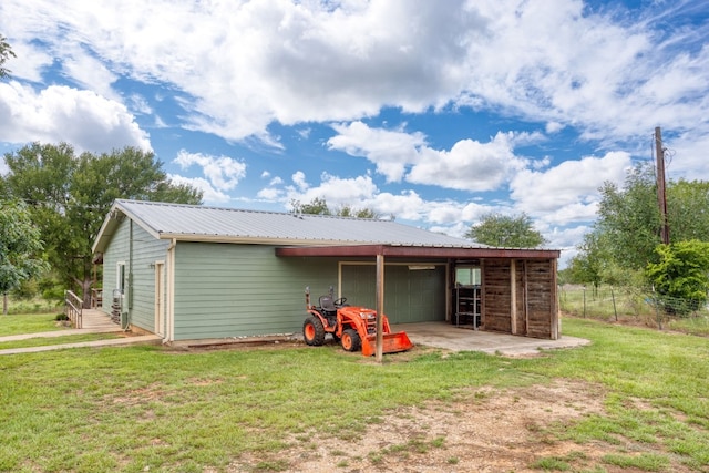 back of property with metal roof, driveway, a detached garage, and a lawn