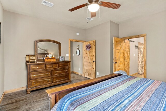 bedroom with dark wood-type flooring, ceiling fan, and a barn door