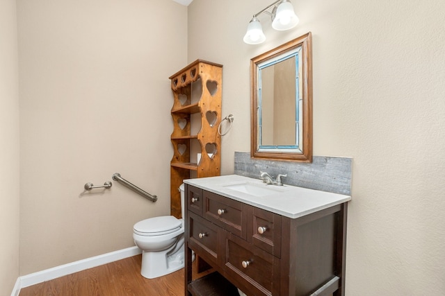 half bath with toilet, wood finished floors, vanity, baseboards, and tasteful backsplash