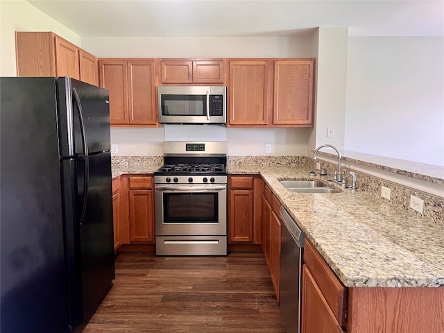 kitchen with sink, dark wood-type flooring, stainless steel appliances, light stone countertops, and kitchen peninsula