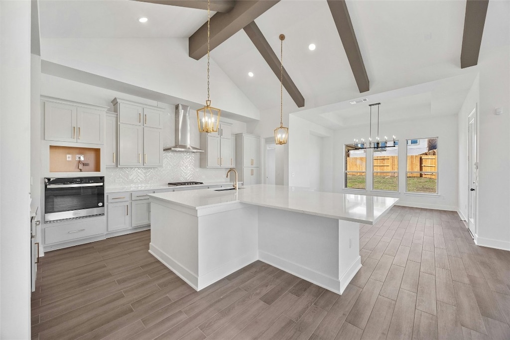 kitchen with an island with sink, light hardwood / wood-style flooring, wall chimney exhaust hood, and oven