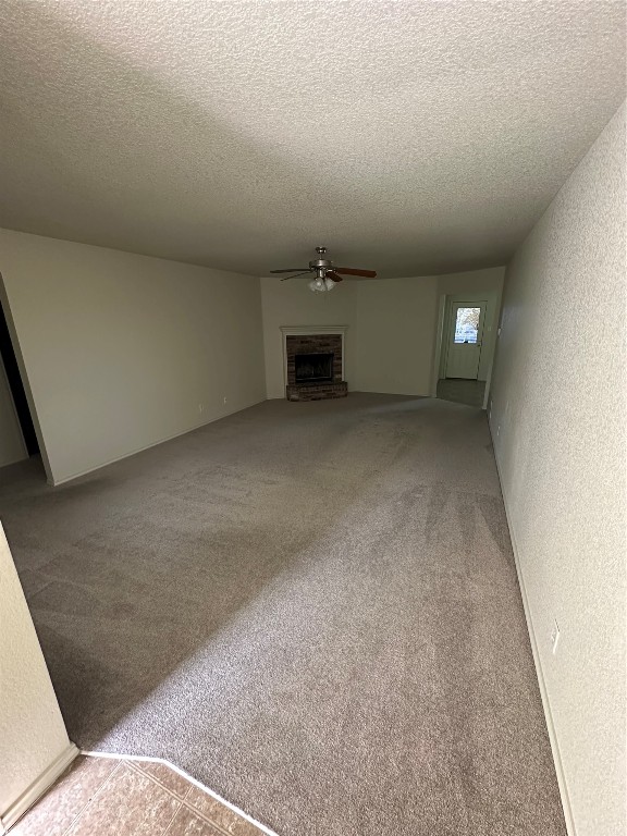 unfurnished living room featuring a fireplace, a textured ceiling, carpet, and ceiling fan