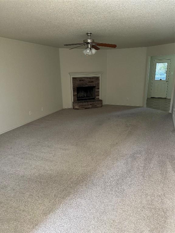 unfurnished living room featuring a textured ceiling, carpet, a brick fireplace, and ceiling fan