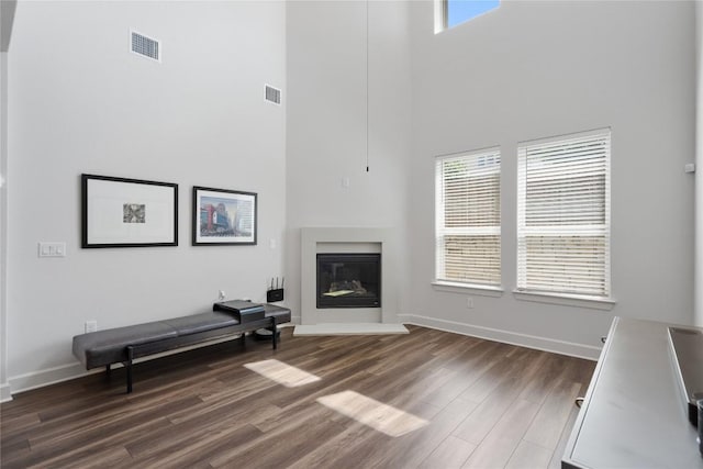 living area featuring a glass covered fireplace, visible vents, dark wood finished floors, and a towering ceiling