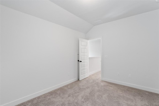 spare room featuring light carpet, vaulted ceiling, and baseboards