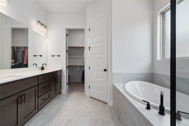 bathroom with a relaxing tiled tub, vanity, and tile patterned flooring