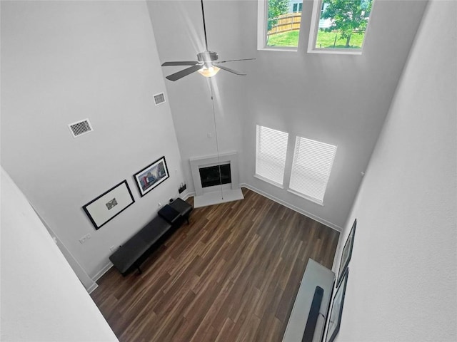 living area featuring dark wood-style floors, visible vents, ceiling fan, and a towering ceiling