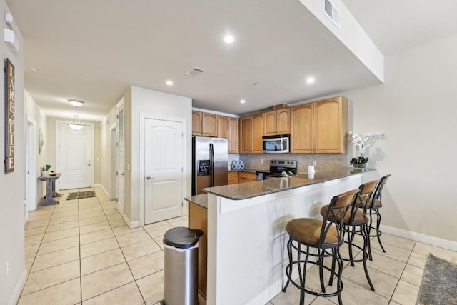 kitchen with light tile patterned floors, a kitchen breakfast bar, stainless steel appliances, kitchen peninsula, and dark stone counters