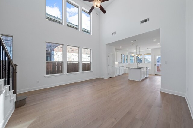 unfurnished living room featuring a high ceiling, light hardwood / wood-style floors, ceiling fan, and sink