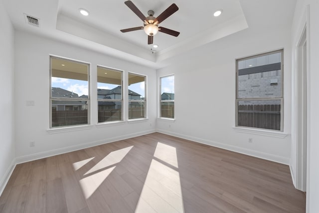 spare room with a tray ceiling, ceiling fan, and light hardwood / wood-style flooring