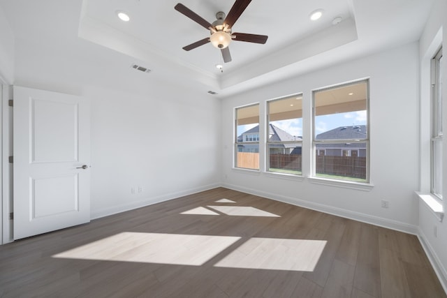 empty room with ceiling fan, a raised ceiling, and dark wood-type flooring