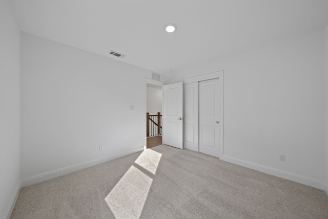 unfurnished bedroom with light colored carpet and a closet